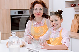 happy grandmother with little granddaughter cooking together and looking