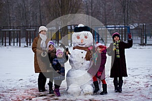 Happy grandmother and many little granddaughters sculpt a big real snowman