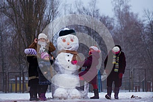 Happy grandmother and many little granddaughters sculpt a big real snowman