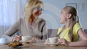 Happy grandmother talking and drinking tea with little cute granddaughter, love