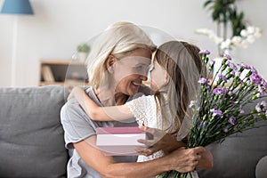 Happy grandmother thanking cute granddaughter for flowers and gi photo