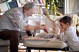 A happy grandpa at home enjoy teaching his little grandson how to play a chess. Family, home, playtime