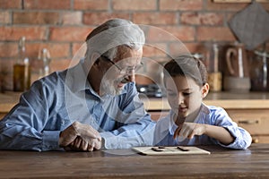 Happy grandpa and little grandson engaged in learning board game