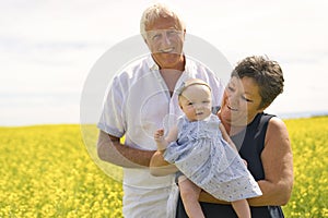 Happy grandparents with little baby granddaughter enjoying moment in beautiful yellow field