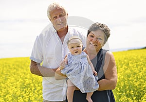 Happy grandparents with little baby granddaughter enjoying moment in beautiful yellow field