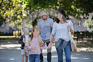 Happy grandparents taking grandchildren home from school, walking outdoors in street.