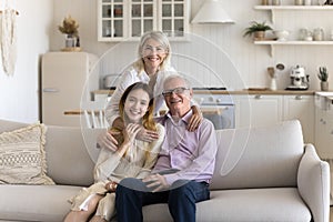 Happy grandparents and teenage girl sitting together on home couch