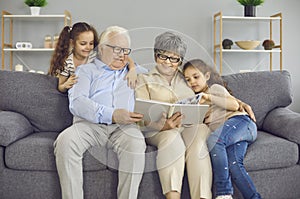 Happy grandparents and their two granddaughters look at a photo book with a family photo together.