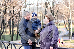 Happy grandparents walking with their little grandson in park