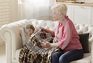 Happy granny covering her granddaughter with warm plaid while she sleeps at home