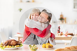 Happy granny hugging granddaughter while cooking traditional holiday turkey for festive family dinner at home