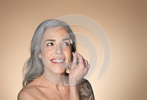 Happy grey-haired senior woman brushing eyebrows with brush and smiling, enjoying beauty routine and cosmetics product