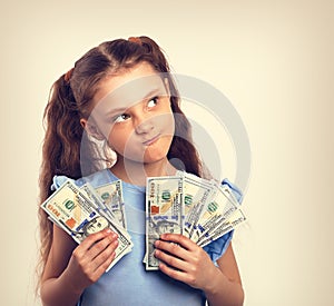 Happy grimacing doubt thinking kid girl holding money in the han