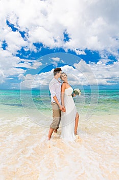 Happy groom and bride having fun on the sandy tropical beach. We