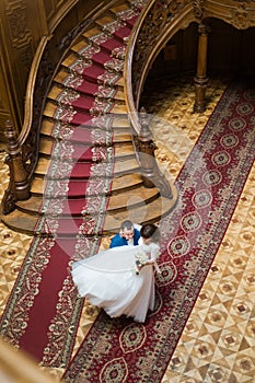 Happy groom carry his wife near big wooden stairs at old vintage house, top view