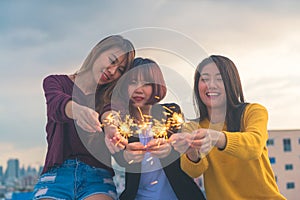 Happy group of asia girl friends enjoy and play sparkler at roof top party at evening sunset.