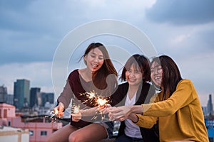 Happy group of asian girl friends enjoy and play sparkler at roof top party at evening sunset,Holiday celebration