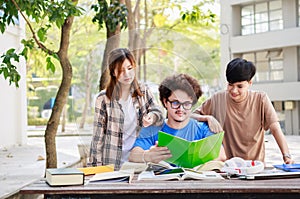 A happy group of attractive young people is tutoring exams with study books, sitting on the study table. Student group and