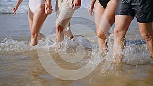 Happy group of barefoot men, women in swimwear at tropical trip come out of sea water, flirt, smile, chat. Cheerful