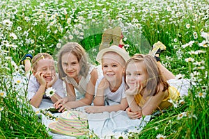 A happy group of children lies in a field of camomiles at sunset in the summer. Boys and girls lie on a blanket in nature, a