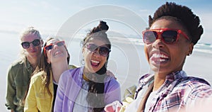 Happy group of diverse female friends having fun, taking selfie with smartphone at the beach