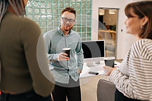 Happy group of ethnically diverse young man and women relaxing while having coffee break at work in light modern office