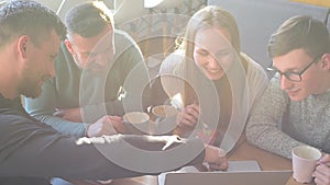 Happy group of friends or business colleagues drinking coffe and laughing and using computer together in a small cafe or