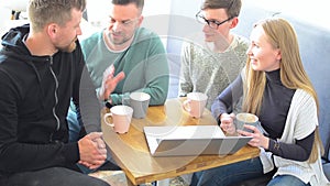 Happy group of friends or business colleagues drinking coffe and laughing and using computer together in a small cafe or