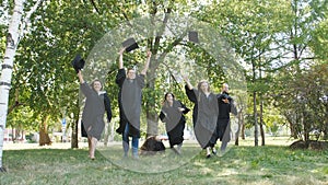 A happy group of graduates on graduation day runs around the park and throws their hats up.