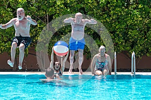 Happy group of mature people enjoying summer and swimming pool, jumping and playing