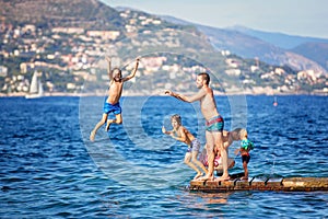 Happy group of people, children and adults, jumping in the water off dock, splashing and having fun