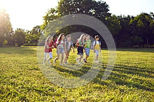 Happy group of schoolchildren have fun in nature outdoors in park on sunny warm day.