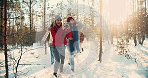 Happy group of smiling multiethnic friends walk along snowy winter forest hike path at holidays weekend slow motion.