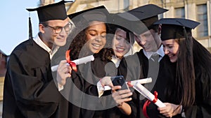 Happy group of students on graduation day laughing at something on mobile phone.