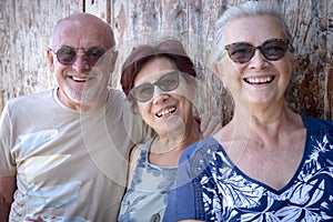 Happy group of three people friends enjoying outdoor excursion standing against a wooden door in a sunny day - active and carefree