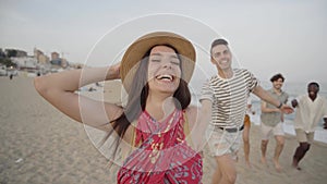 Happy group of young people having fun at the beach. Cheerful friends run holding hands enjoying the summer