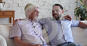 Happy grown son man and older father chatting on couch