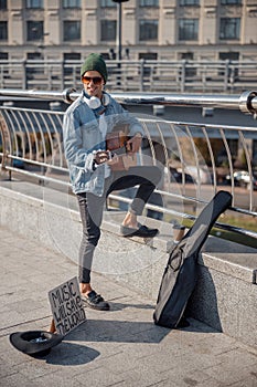 Happy guitarist in hat standing with instrument on the street