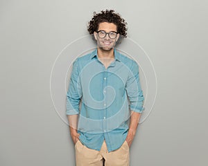 happy guy with glasses in denim shirt holding hands in pockets and smiling