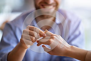 Happy guy holding his fiancee`s hand, putting on engagement ring on her finger, closeup view