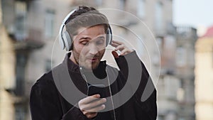Happy guy listening music headphones outside. Smiling man dancing on city street