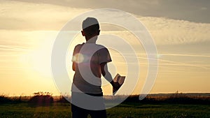 Happy guy playing with a paper airplane in a field in the sun. Silhouette at sunset