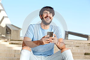 Happy guy sitting outside with mobile phone