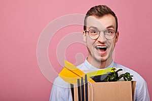 Happy guy in a sky blue shirt and glassesholds cardboard box with things in his hands