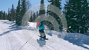 Happy guy snowboarder in color bright jacket and sunglasses on a sunny winter day in the snowy mountains riding a rope