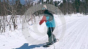 Happy guy snowboarder in color bright jacket and sunglasses on a sunny winter day in the snowy mountains riding a rope