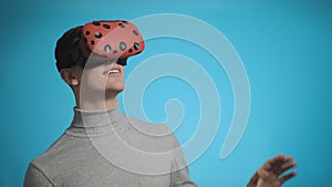 Happy guy with virtual reality glasses waves hand on blue