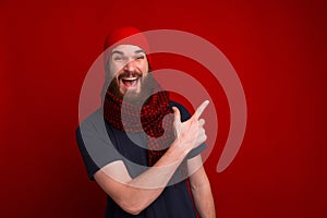 Happy guy wearing red hat and scarf, pointing away while looking