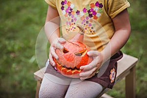 Happy Halloween. Beautiful smiling girl seats on wooden chair and holds little pumpkin Jack O Lanterns outdoors