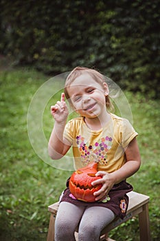 Happy Halloween. Beautiful smiling girl seats on wooden chair and holds little pumpkin Jack O Lanterns outdoors